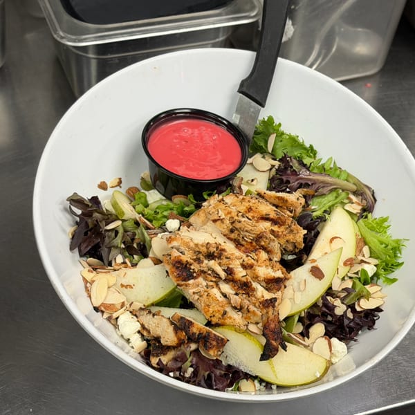 Grilled chicken salad with mixed greens, sliced pears, almonds, feta, and vibrant red dressing.