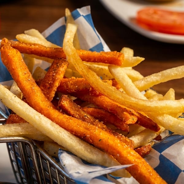 A metal basket filled with a mix of golden french fries and seasoned sweet potato fries.