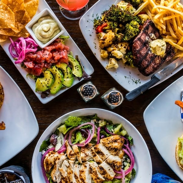 Overhead view of a wooden table laden with various dishes including burgers, steak, salads, and fries.
