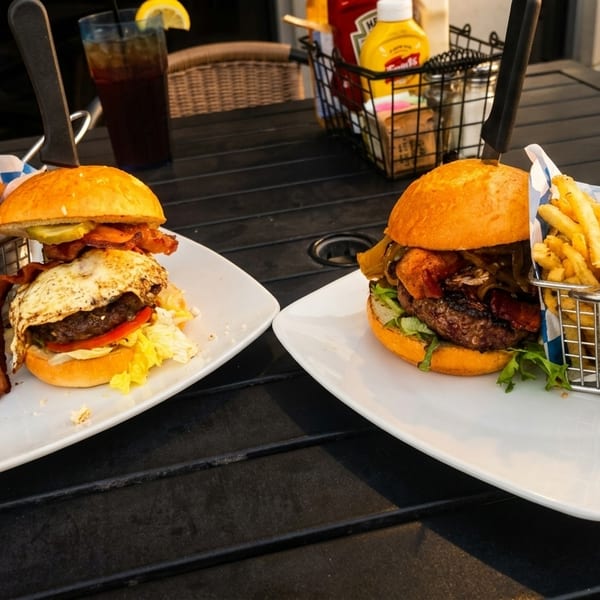 Two gourmet burgers with sides of fries and onion rings on a dark outdoor table.